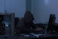 Hacker wearing hoodie with and hacking the system at the office, dark night