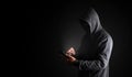 Hacker Using Smartphone. Men in black clothes with hidden face looks at smartphone screen on black background.