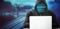 Composite image of hacker wearing black hood while using laptop on table Royalty Free Stock Photo