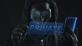 Hacker wearing black mask pulls PRIVATE tab from a smartphone. Hacking concept