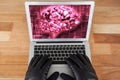 Hacker wearing gloves using a laptop with a pink brain on desktop background