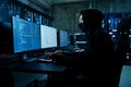 Hacker working on computer with multiple screens in dark room Royalty Free Stock Photo