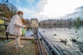 The Hague, The Netherlands - November 10, 2020: Happy elderly senior retired woman with mouth mask. feeds birds bread