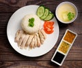 Hainanese chicken rice with soup and three sauces on dark wood table texture