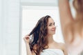 Hair and body care. Woman touching wet hair and smiling while looking in the mirror. Portrait of girl in bathroom applying condit Royalty Free Stock Photo