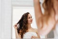Hair and body care. Woman touching wet hair and smiling while looking in the mirror. Portrait of girl  in bathroom applying condit Royalty Free Stock Photo