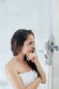 Hair and body care. Woman touching wet hair and smiling while looking in the mirror. Portrait of girl in bathroom applying condit