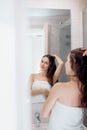 Hair and body care. Woman touching wet hair and smiling while looking in the mirror. Portrait of girl in bathroom applying condit