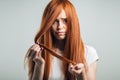 Sad redhead girl holding her damaged hair looking at camera. Royalty Free Stock Photo