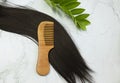 Hair care wooden comb on a long strand of black hair on a white background. Tools from biological materials and natural. hair