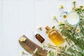 Hair cosmetics. Chamomile flowers and cosmetic bottles of essential oil and extract on white wooden background. Flat lay. Top view Royalty Free Stock Photo