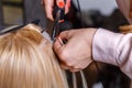 Hair extensions procedure. Hairdresser does hair extensions to young girl, blonde in a beauty salon. Selective focus. Royalty Free Stock Photo