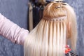 Hair extensions procedure. Hairdresser does hair extensions to young girl, blonde in a beauty salon. Selective focus. Royalty Free Stock Photo