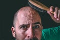 Hair loss concept. Bald man using hair brush on non existent hair. Royalty Free Stock Photo