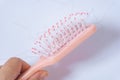 Hair loss problems with hand holding a pink hairbrush on white background. Falling black hair clinging to the comb