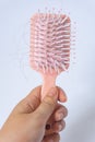 Hair loss problems with hand holding a pink hairbrush on white background. Falling black hair clinging to the comb