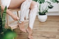 Hair Removal with depilation cream concept. Young woman in white towel applying shaving cream on her legs and holding plastic Royalty Free Stock Photo