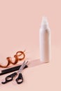 Hair spray bottle with curly lock of hair, scissors and a comb on beige background. Royalty Free Stock Photo