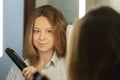 Hair straightening,woman at home with hair iron in bathroom by the mirror