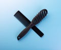Hairbrush and comb crossed on blue background. Pair of black plastic hair combs