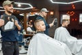 Haircut for little boy. Young smiling barber holding a mirror and showing the result of his work to cute little boy Royalty Free Stock Photo