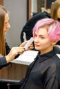 Hairdresser with comb is checking out and fixing the short pink hairstyle of the young white woman in a hair salon. Royalty Free Stock Photo