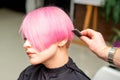 A hairdresser is combing the dyed pink short hair of the female client in a hairdresser salon. Royalty Free Stock Photo