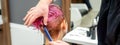 A hairdresser is combing the dyed pink wet short hair of the female client in the hairdresser salon, back view. Royalty Free Stock Photo