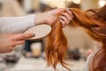 Hairdresser combing her long, red hair of his client in the beauty salon. Royalty Free Stock Photo