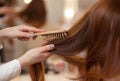 Hairdresser combing her long, red hair of his client in the beauty salon. Royalty Free Stock Photo