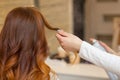 Hairdresser combing her long, red hair of his client and sprinkles hairspray in a beauty salon. Royalty Free Stock Photo