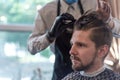 A hairdresser cuts a bearded young guy with a hair trimmer, combing the hair on his head. Work of the master in men`s haircut in Royalty Free Stock Photo