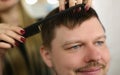 Hairdresser cuts hair with scissors and black comb