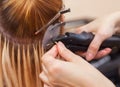 The hairdresser does hair extensions to a young girl, a blonde in a beauty salon.