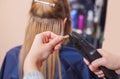 The hairdresser does hair extensions to a young girl, a blonde in a beauty salon