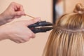 The hairdresser does hair extensions to a young girl, a blonde in a beauty salon.