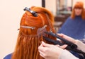 The hairdresser does hair extensions to a young, red-haired girl, in a beauty salon. Royalty Free Stock Photo