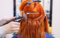 The hairdresser does hair extensions to a young, red-haired girl, in a beauty salon. Royalty Free Stock Photo