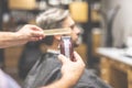 Professional barber holding comb and clipper, client sitting in armchair in the background Royalty Free Stock Photo
