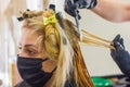 Hairdresser dyes hair in salon, young woman in medical mask in beauty salon