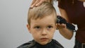 Hairdresser girl cuts the hair of blonde child with an electric trimmer machine. Process cutting hair in barber shop Royalty Free Stock Photo