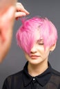 Hairdresser with hands is checking out and fixing the short pink hairstyle of the young white woman in a hair salon. Royalty Free Stock Photo