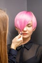 Hairdresser with hands is checking out and fixing the short pink hairstyle of the young white woman in a hair salon. Royalty Free Stock Photo