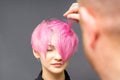 Hairdresser with hands is checking out and fixing the short pink hairstyle of the young white woman in a hair salon. Royalty Free Stock Photo