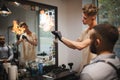 A delightful barber spraying fire flames with a hairspray and tools for beard shave on a barbershop background.