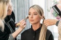 A hairdresser and a makeup artist together do styling and makeup for a young and beautiful model girl in a beauty salon. Royalty Free Stock Photo