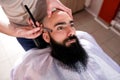 Hairdresser shaves man beard with a blade in a male
