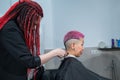 The hairdresser shaves the temple of a female client. Asian woman with short pink hair in barbershop.