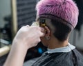 The hairdresser shaves the temple of a female client. Rear view of a woman with short pink hair in a barbershop.