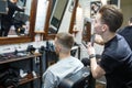 Hairdresser shows short haircut with mirror to handsome satisfied client in professional hairdressing salon